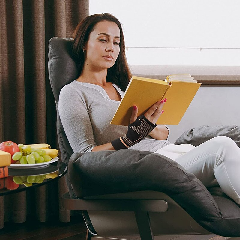 Woman reading a yellow book in a comfortable chair with fruit on a table beside her.