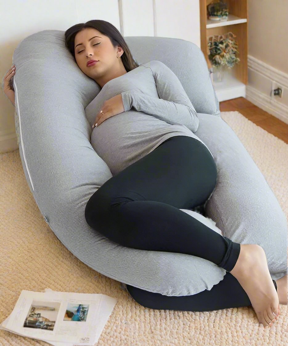 Pregnant woman using a U-shaped body pillow in a home setting.