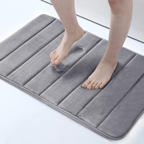 Person stepping onto a gray bath mat on a light background